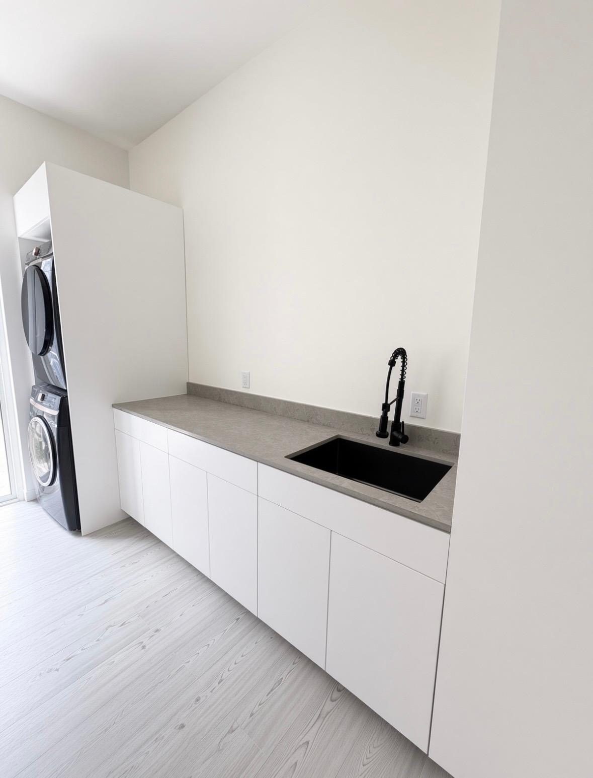 Separate laundry room with stacked washer and dryer, white cabinetry, worktop and sink